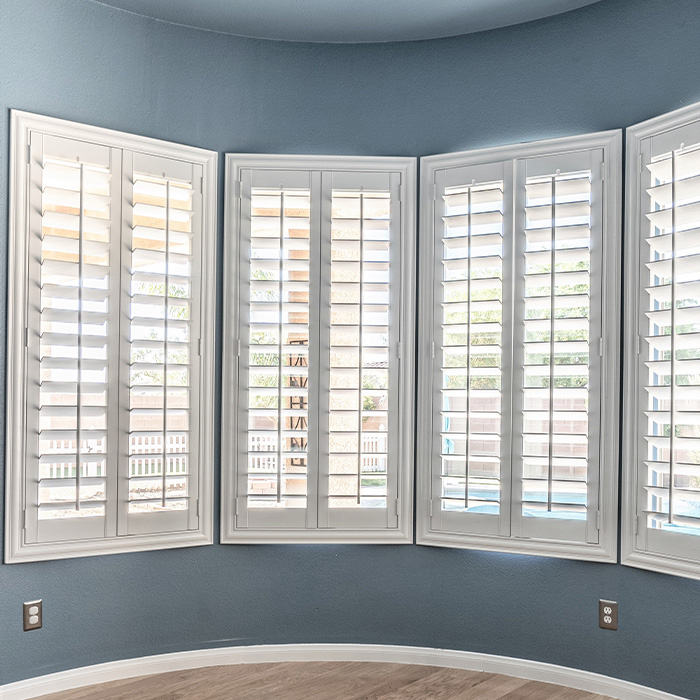 White eyebrow shutters in a bay window style within a living room.