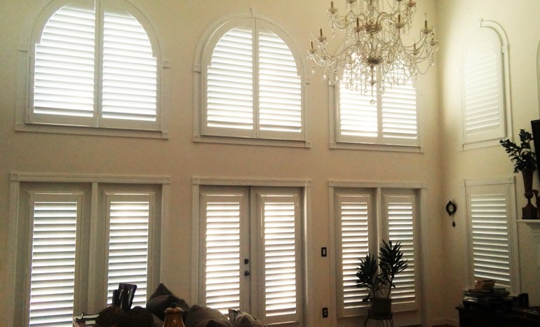 Entertainment room in open concept Dover house with plantation shutters on arch windows.